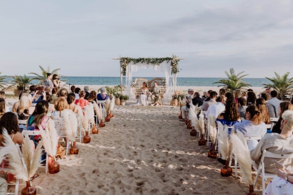 Ceremonia de boda estilo boho en la playa con pampas, macramé y sillas blancas frente al mar en DBlanc.