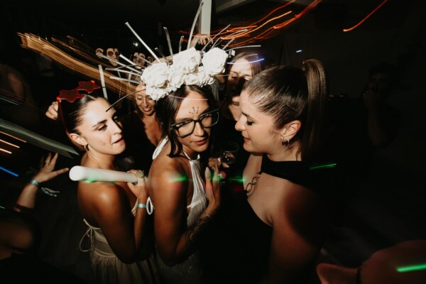 Novia e invitadas celebrando la fiesta de boda con accesorios divertidos y luces dinámicas en la pista de baile de DBlanc.