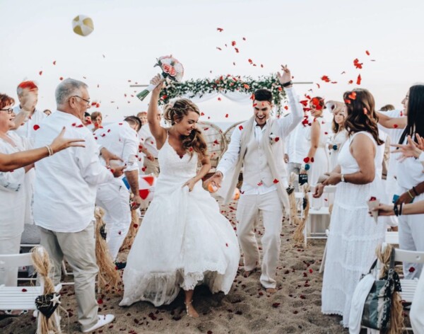 Recién casados celebrando la salida de la ceremonia con lluvia de pétalos rojos en la playa de DBlanc.