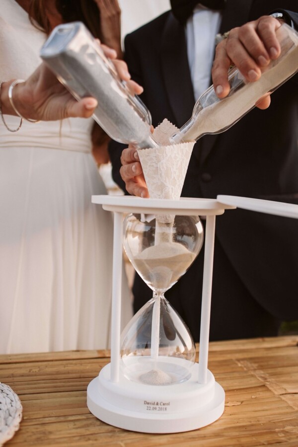 Novios realizando el ritual de la arena con botellas de cristal en una ceremonia de boda frente al mar en DBlanc.